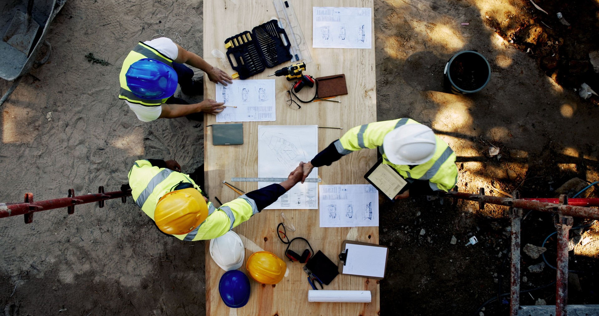 Blueprint, architecture and men at table shaking hands for collaboration, agreement and inspection from above. Construction, building team and contractor on site with floor plan, handshake and deal
