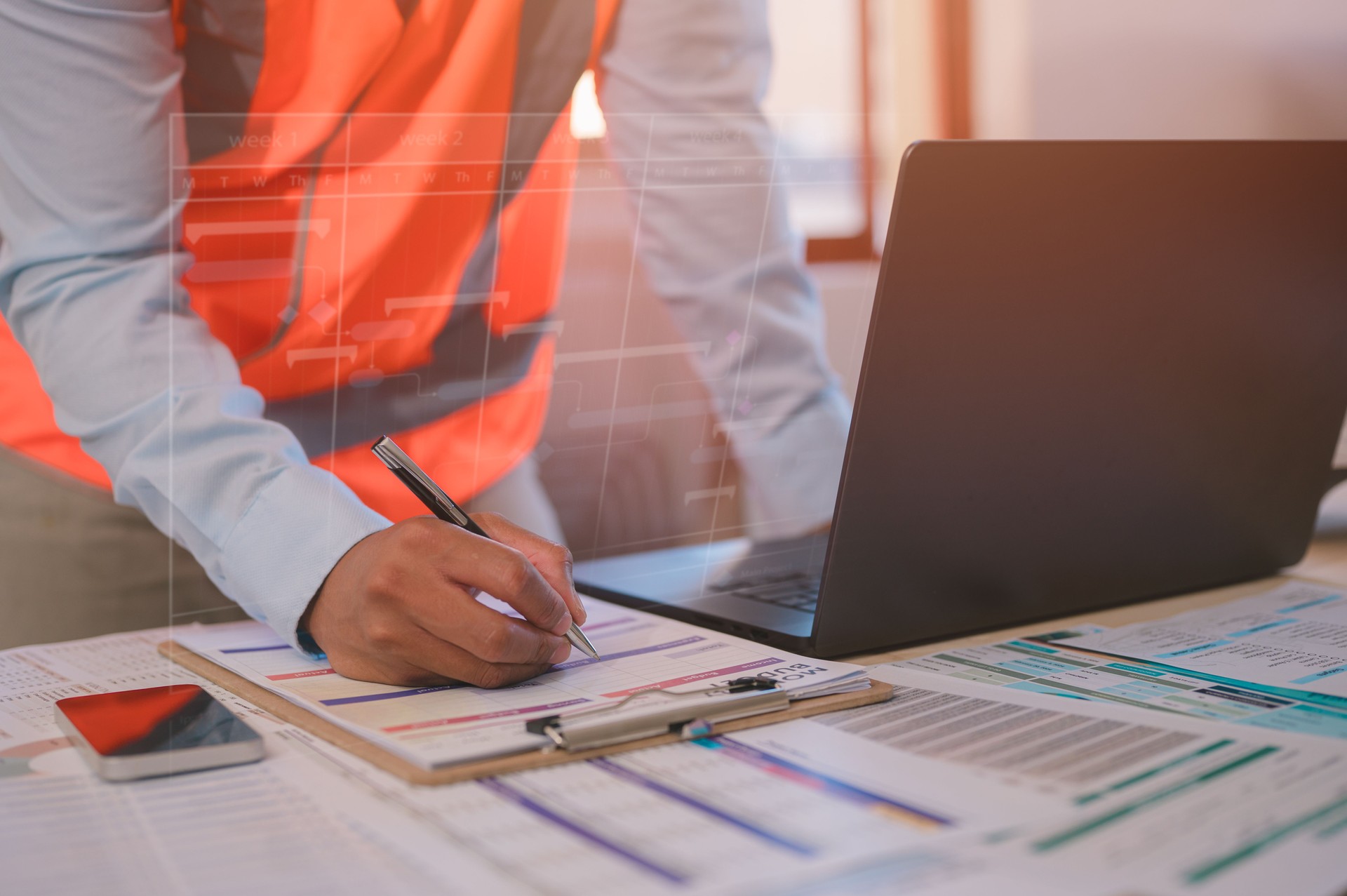 An engineer or foreman working on site sitting on desk in office using pen and computer analysing data charts paper work
